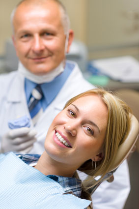 A woman smiling in the dental chair next to her dentist